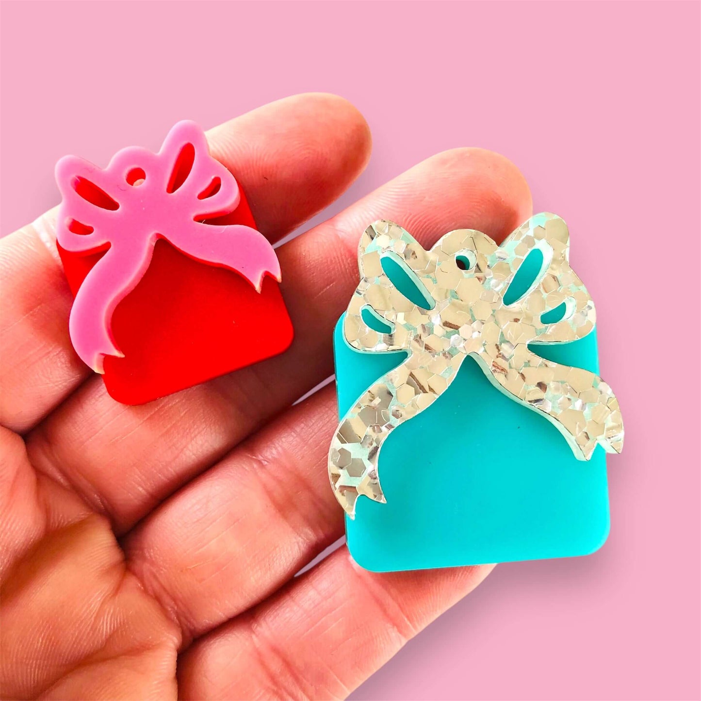 Hand holding Pretty Package Duo with red and pink bow gift box, and blue and silver bow gift box against a pink background.